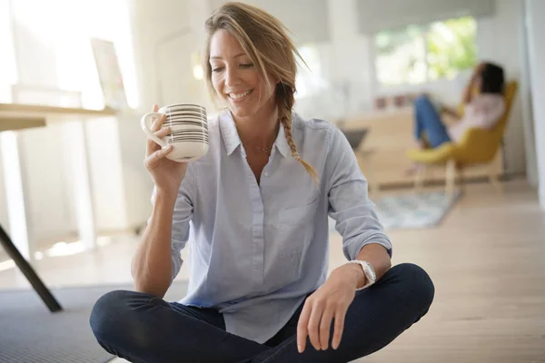 Beautiful 30-year-old woman drinking hot tea, sitted on floor