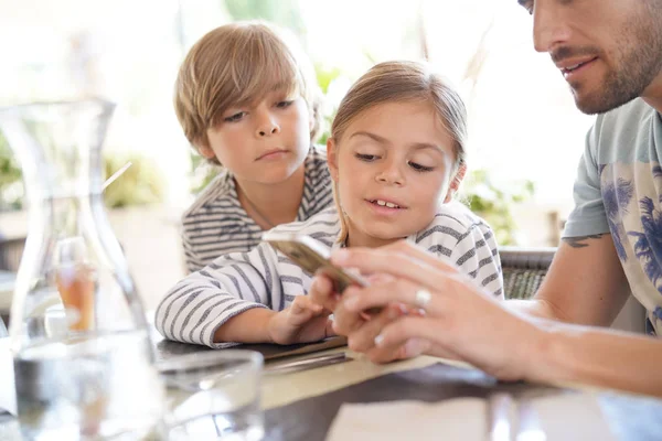 Father with kids playing with smartphone at restaurant