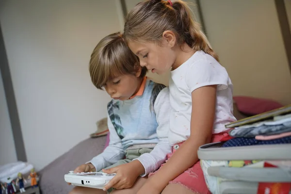 孩子们玩电子游戏坐在床上 — 图库照片