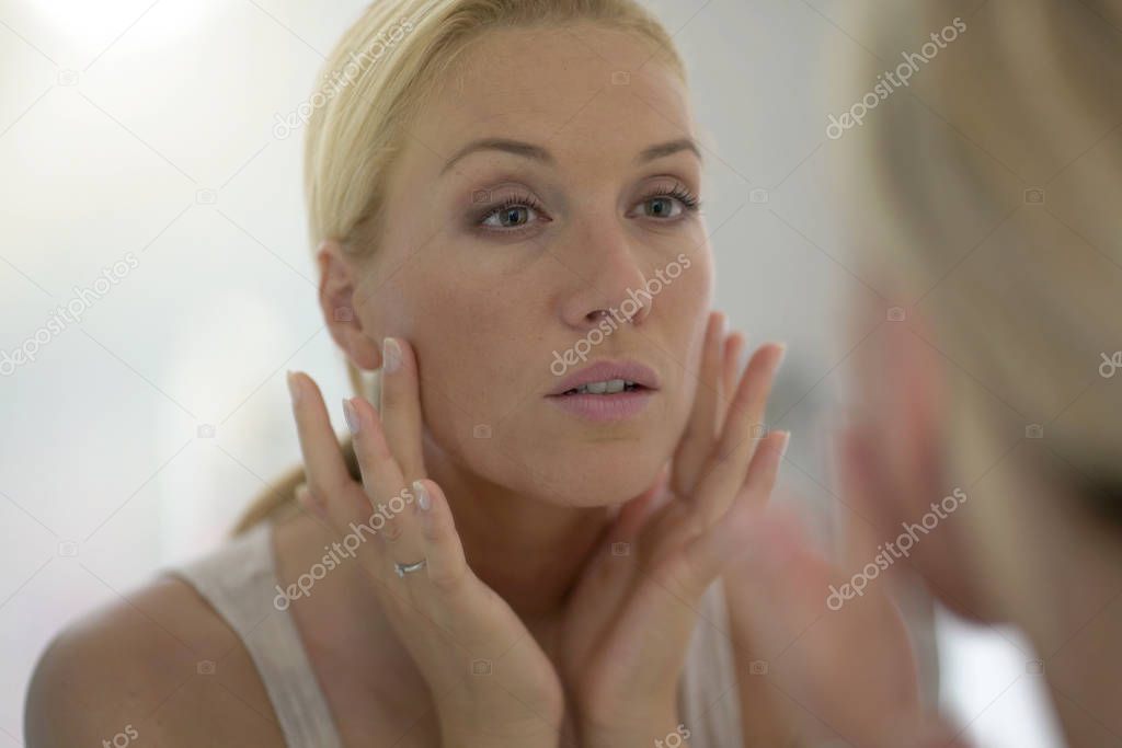 40-year-old woman looking at her face in mirror