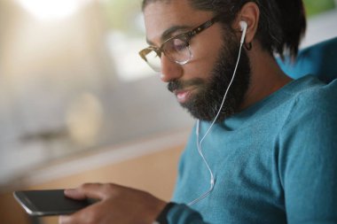 Akıllı telefon ve kulaklık kullanarak koltukta oturan adam