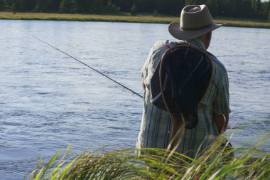 Gün batımında nehir kenarında oturan balıkçı.