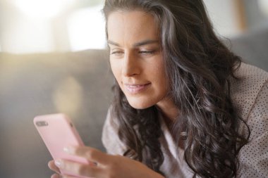 Esmer kadın kanepe üzerinde rahatlatıcı smartphone ile bağlı
