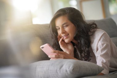 Esmer kadın kanepe üzerinde rahatlatıcı smartphone ile bağlı
