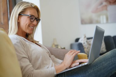 Sarışın kadın kanepe, rahatlatıcı bağlı dizüstü bilgisayar ile