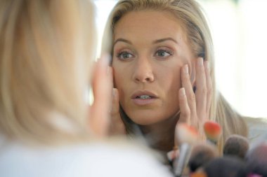 Orta yaşlı kadın teninin ayna önünde bakarak