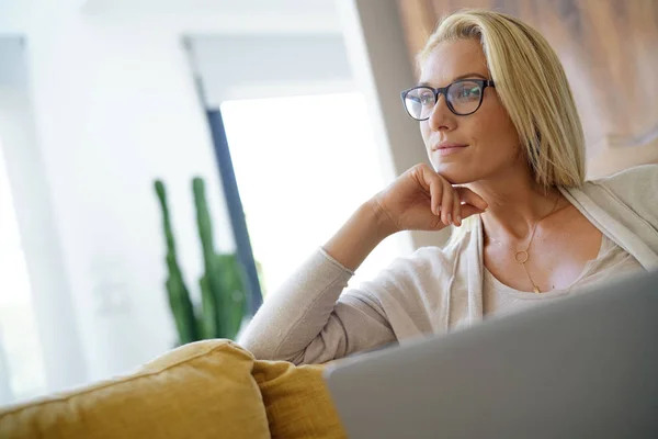 Blond woman relaxing in sofa, connected with laptop