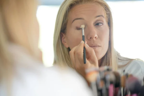 Woman in front of mirror applying eyeshadow