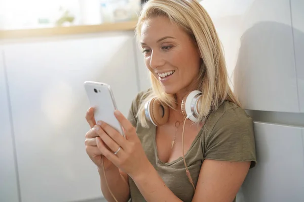 金发女子连接与智能手机和使用耳机 — 图库照片