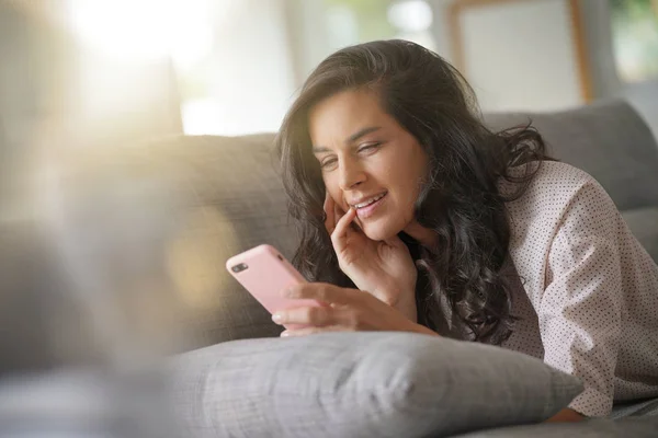 Brunette woman relaxing on sofa, connected with smartphone
