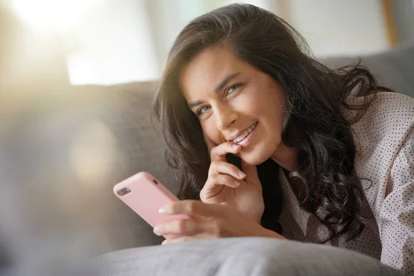 Brunette woman relaxing on sofa, connected with smartphone