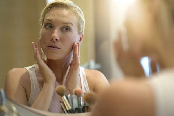 40-year-old woman putting makeup on in front of mirror