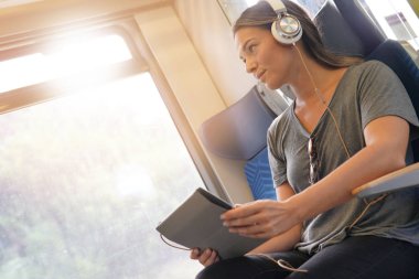 Tablet ve kulaklık ile tren ile seyahat eden genç kadın                              