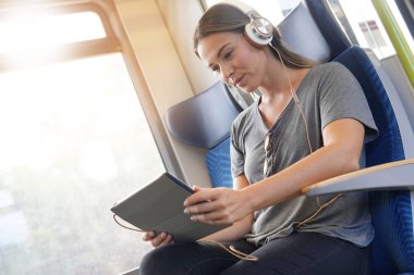 Tablet ve kulaklık ile tren ile seyahat eden genç kadın                              