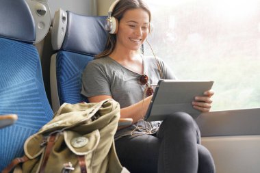 Tablet ve kulaklık ile tren ile seyahat eden genç kadın                              