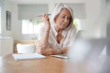  Evde bilgisayar üzerinde çalışan yaşlı kadın                              