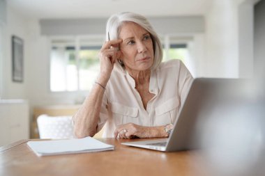  Evde bilgisayar üzerinde çalışan yaşlı kadın                              