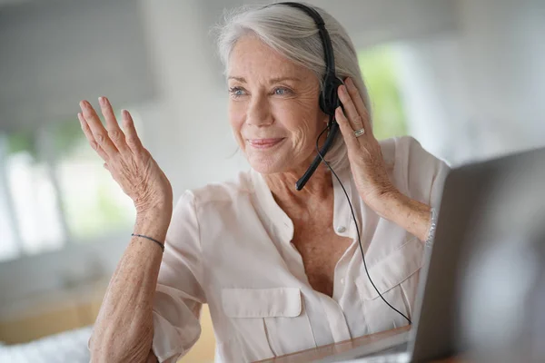 Seniorkvinne Som Arbeider Datamaskin Med Hodetelefoner – stockfoto