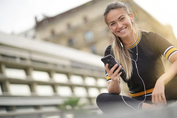 彼女の携帯電話とイヤフォンの町に座っている若い女性 — ストック写真