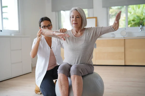 Senior woman exercising with her physiotherapist and swiss ball