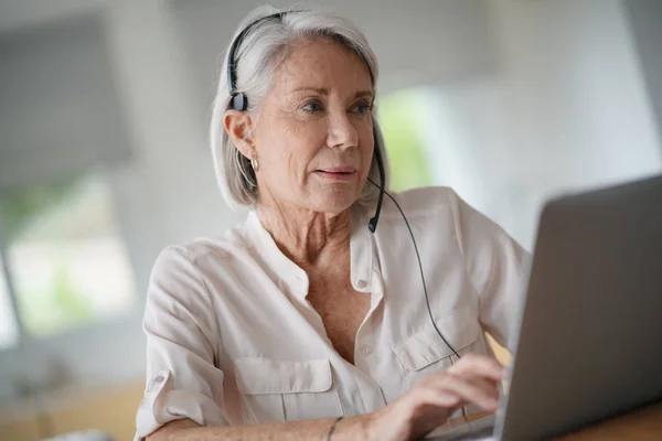 Seniorkvinne Som Arbeider Datamaskin Med Hodetelefoner – stockfoto