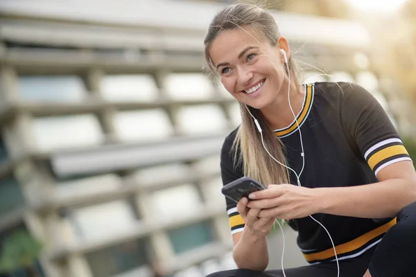 若い女性が屋外に座って 彼女の携帯電話を保持しながら笑みを浮かべて — ストック写真