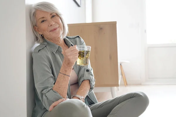 Attractive senior woman sitting on the floor at home with tea