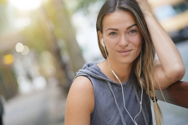 A young woman with earbuds looking relaxed in a city setting and looking at the camera