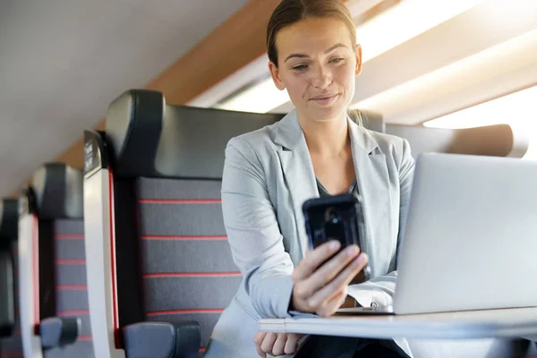 Businesswoman working on train and smiling at cellphone