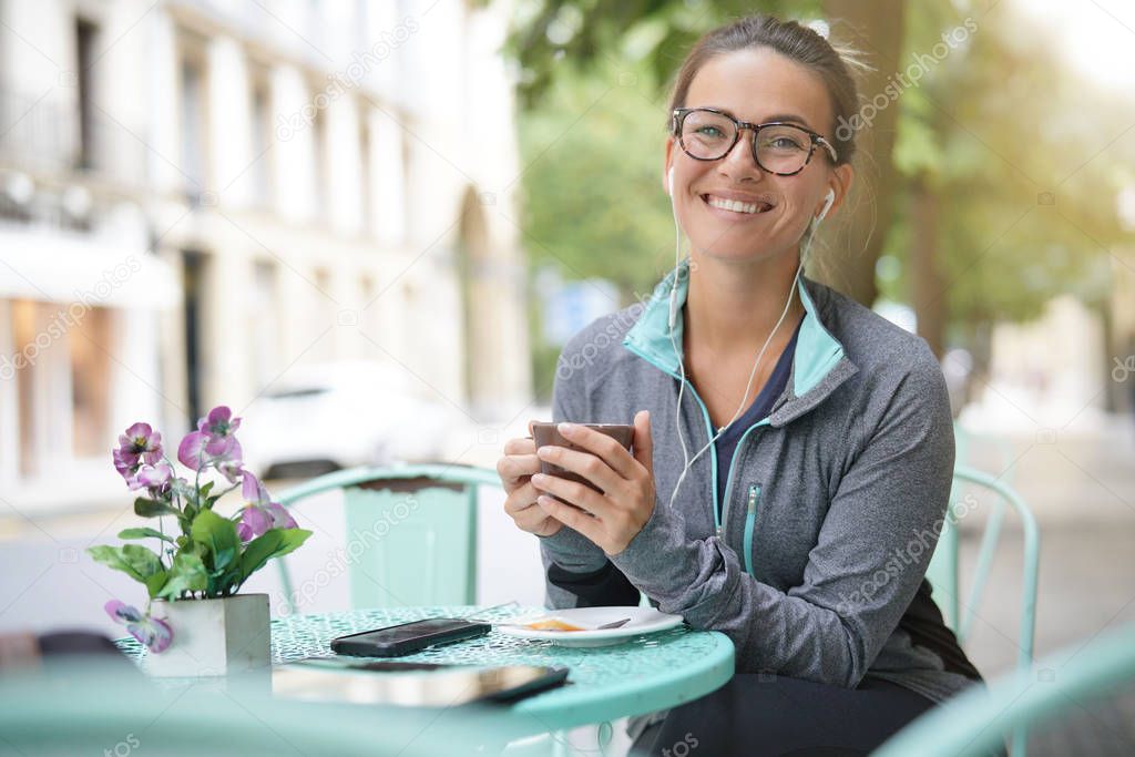  Woman sitting outisde of a coffee shop with headphones and devices                              