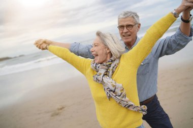  Lively senior couple playing around on beach together                               clipart