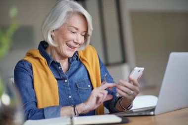Çekici kadın kıdemli gülümseyen, evde çalışan iken mesaj                               