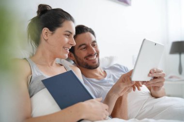 Çekici çift okuma ve kitap ve tablet ile yatakta rahatlatıcı