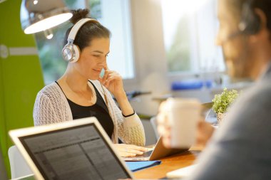 Ofis çalışma işbirliği çalışma kulaklık giyen çekici kadın