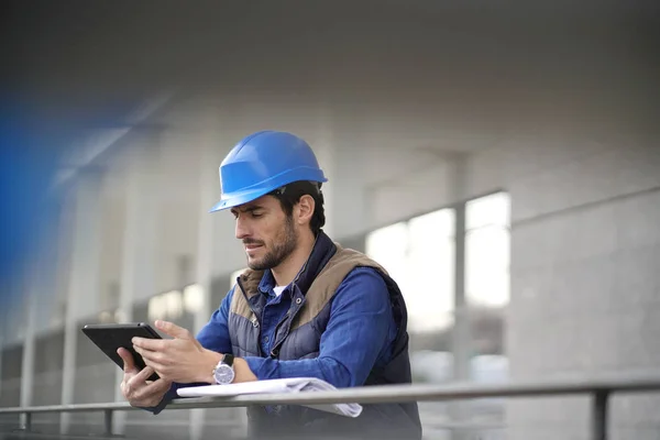 Handsome building expert in hardhat outdoors with tablet and blueprint