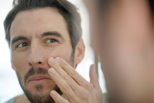 Bonito Homem Aplicando Creme Facial Olhando Espelho — Fotografia de Stock