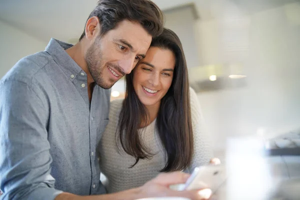 Stunning couple happily looking at cellphone in kitchen