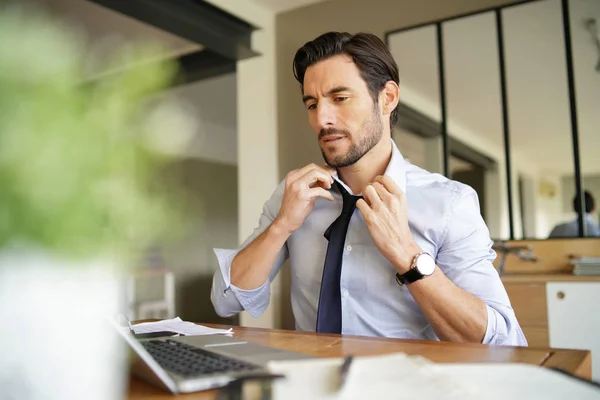 Relaxed attractive businessman undoing tie and working in modern office