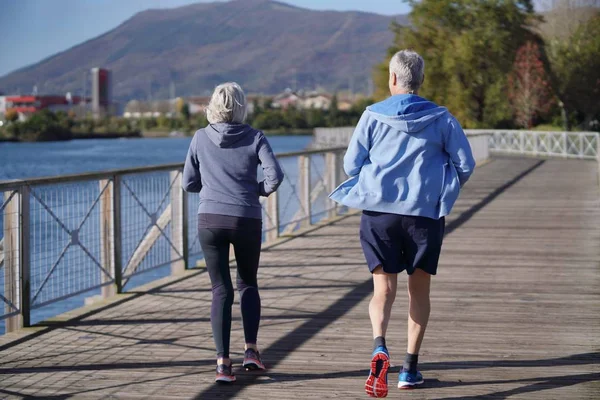 Active senior couple jogging together on bridge
