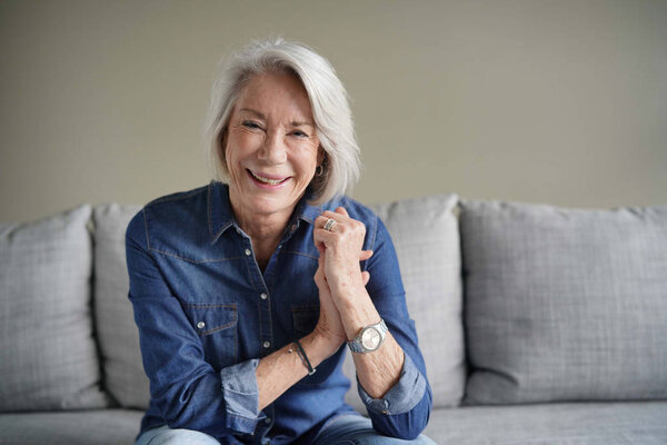  Portrait of modern senior woman laughing in all denim on couch                              