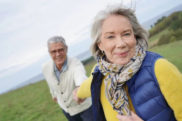 健康的老年妇女牵着丈夫的手走在农村散步的前列 — 图库照片