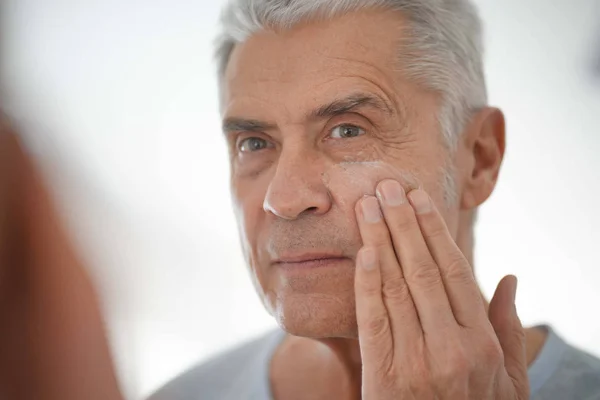 Bonito Homem Sênior Aplicando Creme Facial Espelho — Fotografia de Stock