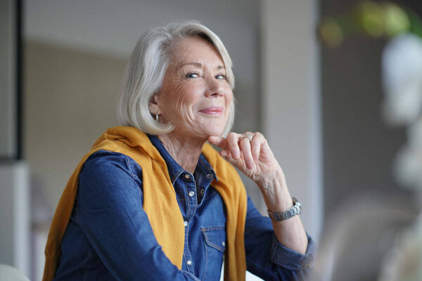  Красивая пожилая женщина выглядит задумчиво дома с ноутбуком
                              