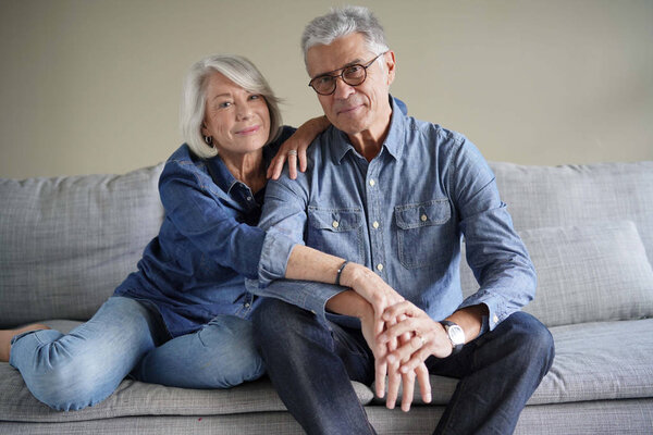 Modern senior couple in denim on couch looking at camera                               