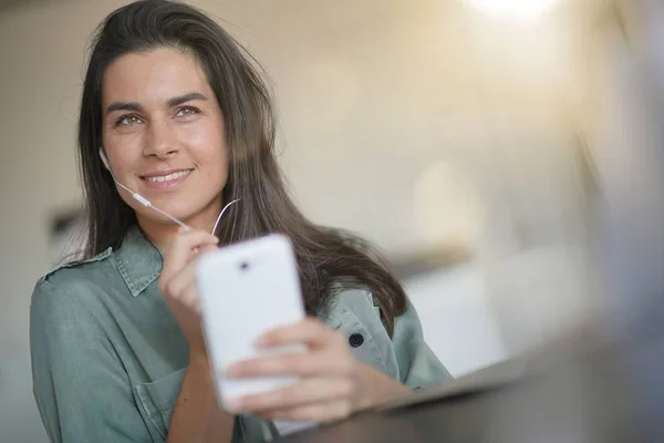 Beautiful brunette talking on cellphone with headphones at home