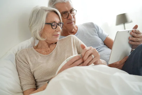 Casal Sénior Relaxante Cama Olhando Para Tablet — Fotografia de Stock