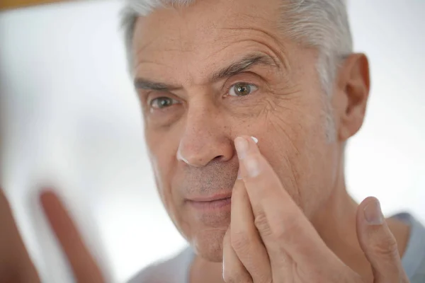 鏡の中の顔のクリームを適用するハンサムな年配の男性 ロイヤリティフリーのストック画像