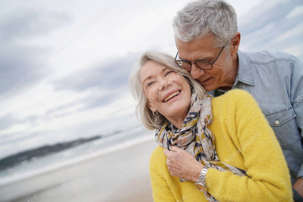 Portrait of attractive vibrant senior couple embracing on beach in fall                              