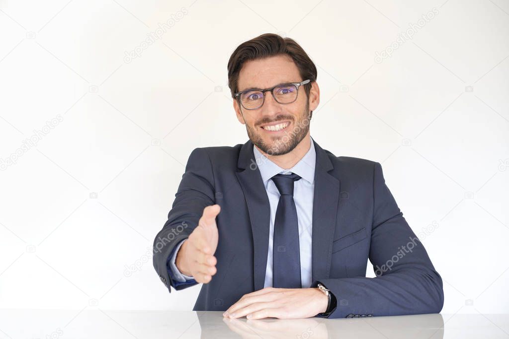 Isolated attractive businessman sitting at desk in suit with extended arm