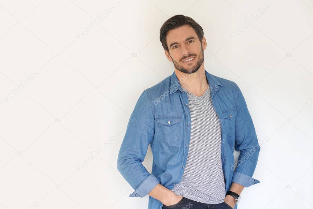 Very handsome casual man smiling and standing with hands in pocket on white background
